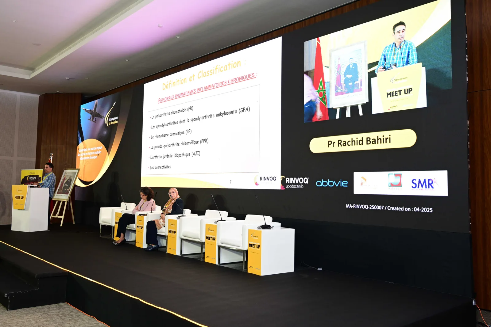 Conférence avec grand écran de présentation et panel sur scène.