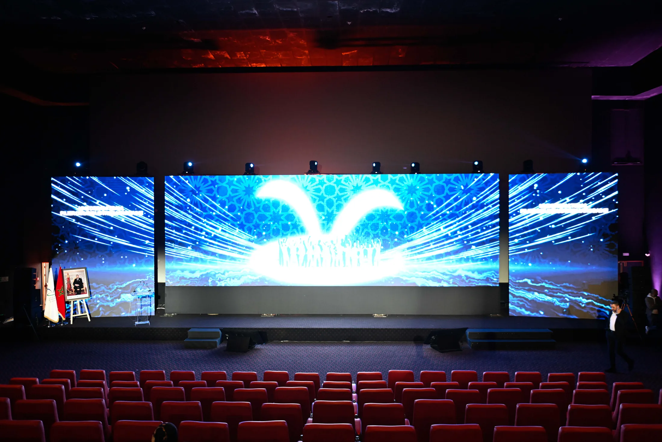 Grande scène intérieure avec écran LED panoramique et rangées de sièges.